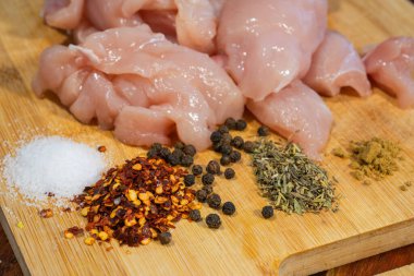  Çiğ tavuk parçaları ve tuz, biber taneleri, biber, kurutulmuş otlar ve ahşap kesim tahtasındaki yer baharatı gibi çeşitli baharatlar..