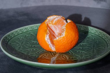 Kısmen soyulmuş bir portakal, karmaşık çiçek ve geometrik desenli dekoratif yeşil bir plakanın üzerinde oturur..