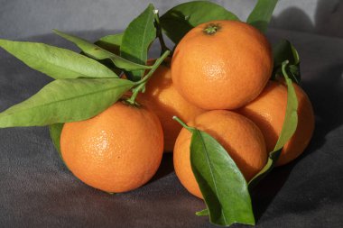 Yeşil yapraklı canlı mandalinalar yumuşak, siyah bir arkaplana karşı yeşil bir tabakta dinleniyorlar..