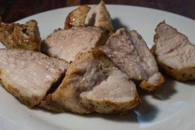 Beyaz bir tabakta kavrulmuş domuz eti dilimleri, kahverengi bir kabuk ve sulu bir iç mekan sergiliyor..