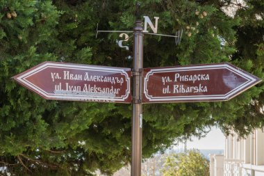 İki dilli bir sokak levhası ve yönlü oklar açık havada bir pusula tepesinin altında duruyor..