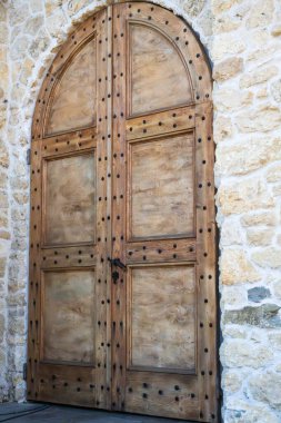 Üzerinde siyah metal çiviler olan büyük kemerli ahşap bir kapı kırsal taştan bir duvarda duruyor..