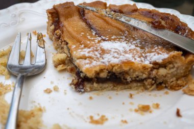 Bir çatal ve bıçağın yanındaki beyaz tabakta pudra şekerle tozlanmış yarısı yenmiş armut turtası..