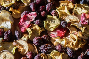 Kurumuş elma dilimleri ve parlak güneş ışığıyla aydınlatılan kırmızı gül kalçalarının dokulu arkaplanı..