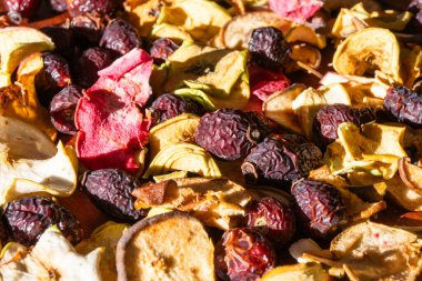 Kurumuş elma dilimleri ve parlak güneş ışığıyla aydınlatılan kırmızı gül kalçalarının dokulu arkaplanı..