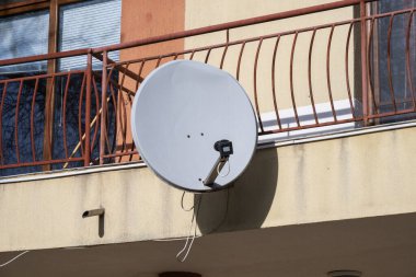 Beyaz dairesel uydu anteni bir yerleşim yerinin bej dış duvarına monte edilmiş.,