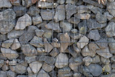 Düzensiz gri taşlardan oluşan bir gabion duvarın desen görüntüsü metal tel örgülerin arkasında sıkıca paketlenmiş..
