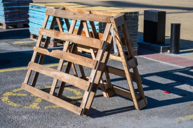 Asfalt üzerinde ahşap çerçeveli barikat, sarı zemin işaretleri ve mavi paletler ve inşaat malzemeleriyle.