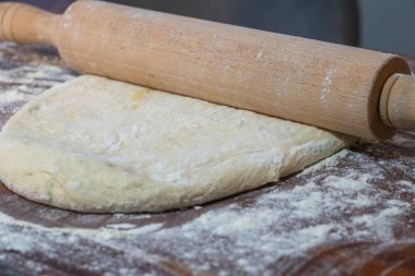 Tahta bir oklava. Beyaz hamuru yassılaştırıyor. Koyu ahşap bir yüzey üzerinde..