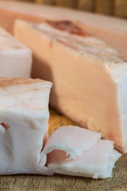 Ahşap bir tahtanın üzerinde duran kalın, çiğ domuz yağı blokları, ince talaşlar ortaya koyuyor domuz yağının pürüzsüz, beyaz dokusu.