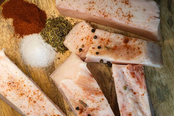 Biber soslu çiğ domuz eti dilimleri, ahşap bir tahtaya dizilmiş kırmızı biber yığınları, kurutulmuş otlar ve beyaz tuz..