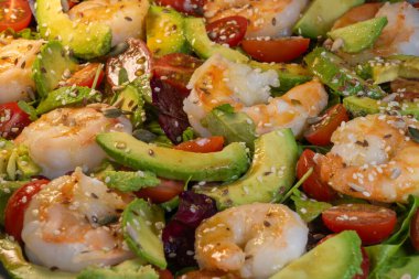 a nutrient-rich shrimp and avocado salad, featuring cherry tomatoes and mixed greens, all generously topped with flax and sesame seeds.