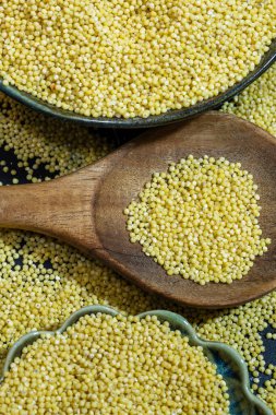 Koyu sarı darılarla dolu ahşap bir kaşık, koyu yeşil bir kâse ve açık yeşil bir kase arasında dinleniyor..