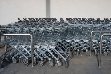 Gri metal alışveriş arabaları, düz beyaz bir duvara karşı, belirlenmiş bir körfezde bir araya toplanmış..
