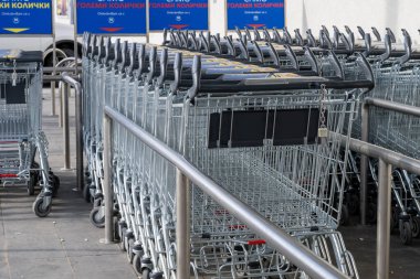 Uzun bir sıra metal alışveriş arabaları arka planda mavi levhalarla süpermarketin dışında bir ağılda bir araya toplanmış..