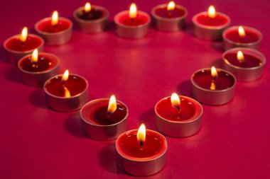 Katı kırmızı arka planda kalp şeklinde dizilmiş çoklu ışıklandırma mumlarını yakar.