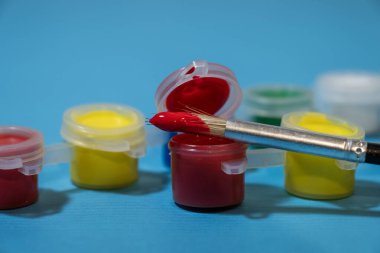 Boya fırçasıyla boyanmış küçük renkli boya kaplarından oluşan bir şerit. Ucu kırmızı boyayla kaplanmış. Açık kırmızı konteynırın üzerinde duruyor..