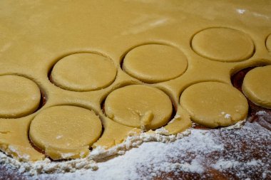 Katlanmış çiğ kurabiye hamuru, içinde birkaç dairesel şekil kesilmiş, un tozlu bir yüzey üzerinde pişmeye hazır..