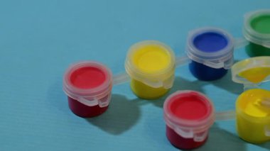 Bir boya fırçası mavi arka plandaki renkli plastik kaplar içinde küçük bir kap sarı boyaya batırılıyor..