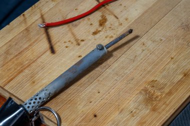 Kullanılmış bir lehim demirinin arka planda kırmızı bir telle birlikte koyu renk yanık izleri olan açık ahşap bir tahtanın üzerinde dinlenmesi..