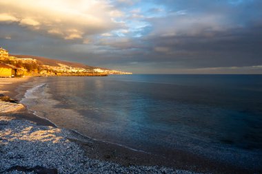 Batan güneşin altın ışığının kumlu sahil ve kıyı binalarını aydınlattığı eğri bir sahil şeridi. Karanlık, kasvetli deniz ve tepemizde ağır gri bulutlarla çelişen Bulgaristan ve Nessebar.