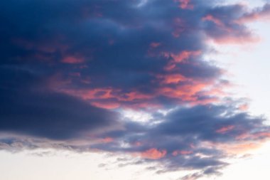 Karamsar, karamsar, mor ve mavi bulutlarla dolu dramatik bir gökyüzü batan güneşin yumuşak pembe ve turuncu renkleriyle aydınlatılıyor..