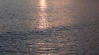 Gün batımında denizin yumuşak dalgalanan yüzeyinde parıldayan altın güneş ışığı parlak bir ışık yolu oluşturur..