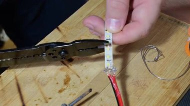 Elleri siyah tel kesiciler kullanarak LED bir şeridi tam olarak kesmek için tahtadan bir tezgah üzerinde belirlenen kesme hattı boyunca.