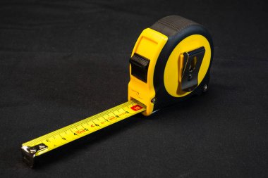 Sarı ve siyah şeritli bir mezura. Sarı metal şeridi kısmen genişletilmiş, koyu siyah bir zemin üzerinde duruyor..