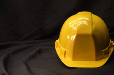 Parlak sarı bir şapka örtülü siyah bir kumaş arka planda duruyor. Stüdyonun kıvrımlı plastik kabuğundaki yansımalarını gösteriyor. Sol tarafında boşluk var.