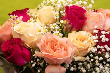 Parlak yeşil arka planda kırmızı, şeftali ve kremalı güllerle küçük beyaz papatyalar ve bebek nefesi karışımı canlı bir çiçek aranjmanı..