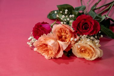 Kırmızı, şeftali ve krema güllerinden oluşan yemyeşil bir düzenleme. Bebeğin nefesi hassas ve pembe arka planda..