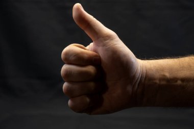 Katı siyah bir arkaplana karşı baş parmak işareti yapan bir el..