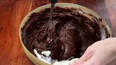 Metal çırpıcı kullanarak beyaz kremayı kalın, zengin bir çikolata hamuruna katlayan biri..
