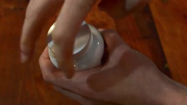 Beyaz plastik bir şişenin vidalarını söken ve portakal rengi oval hapları ahşap bir masanın üzerine döken eller..