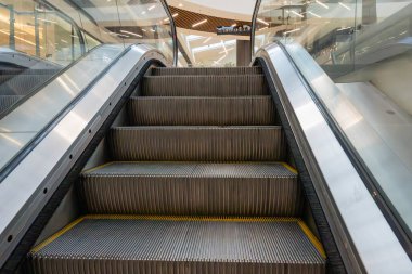 modern bir yürüyen merdiven, sarı güvenlik kenarları ve cam balyaları ile parlak bir üst kata doğru uzanan yivli gümüş basamakları vurguluyor.