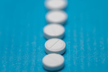 Beyaz yuvarlak tabletlerden oluşan dikey bir sıra ortadaki çizgiler, arka planı bulanıklaştıran sığ bir alan derinliği olan dokulu mavi bir yüzey üzerinde düzenlenmiş..