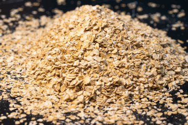 Koyu bir zemin üzerinde yuvarlanmış çiğ, tam tahıllı yulaf taneleri, sağlıklı kahvaltı malzemelerini ve doğal yiyecekleri vurguluyor.