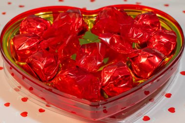 İçi altın kaplamalı, kırmızı folyoya sarılı ve beyaz bir yüzey üzerinde kalp konfetisiyle çevrili kalp şeklinde bir kutu..