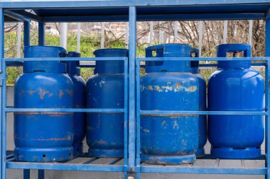 Mavi metal bir kafes yapısında güvenli bir şekilde depolanmış propan ya da bütan tankları gibi büyük bir mavi metal gaz silindiri grubu..