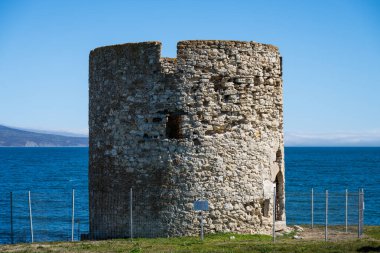 Bir ortaçağ taş kulesi derin mavi bir deniz ve açık bir gökyüzü olan Nesebar, Bulgaristan 'da çimenli bir kıyıda duruyor.