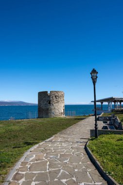 Bulgaristan 'ın mavi denizi manzaralı tarihi taş kuleye doğru park banklarını ve klasik bir sokak lambasını geçerek giden taştan bir yol.