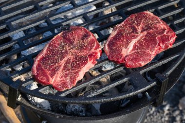 İki çiğ, baharatlı bifteği siyah ızgara ızgaraya koyup sıcak kömür ve beyaz külün üzerinde pişirmeye başladılar..