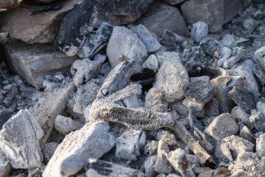 Gri ahşap küllerinin, kömür parçalarının ve küçük taşlarla karıştırılmış beyaz közlerin karmaşık dokularını gözler önüne seren soğuk bir ateş çukuru..