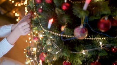Noel ağacını süsleyen çocukların yakın çekimleri. Arka planda parlak şenlik ışıklarının topları var. Çocuklar Noel ağacı süslüyorlar.