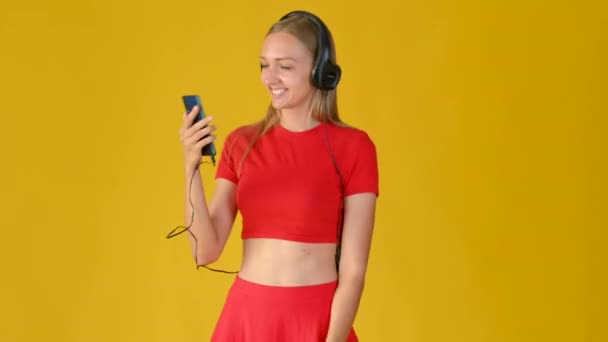 Aantrekkelijk Meisje Met Koptelefoon Een Smartphone Glimlacht Kiest Melodieën Jonge — Stockvideo