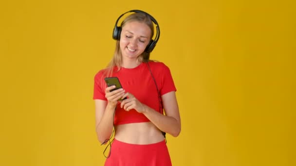 Kulaklıklı Akıllı Telefonlu Gülümseyen Melodileri Seçen Çekici Bir Kız Genç — Stok video