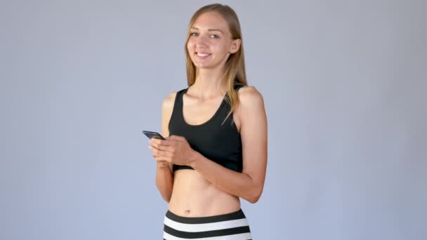 Spor Kıyafetli Genç Kız Gülümsüyor Telefonu Kullanıyor Kadın Beyaz Arka — Stok video