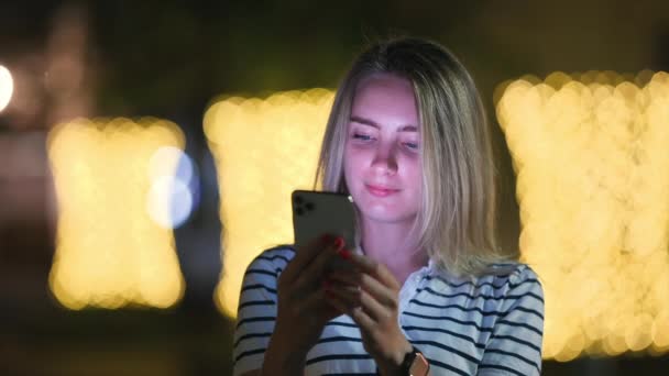 Симпатичная Девушка Использует Смартфон Улыбки Стоящие Ночной Улице Городе Сообщения — стоковое видео