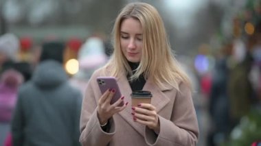 Bir fincan sıcak kahveli genç bayan şehirde sokakta dururken cep telefonu kullanıyor..